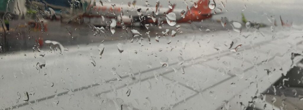 Seitlicher Blick aus dem Flugzeugfenster. Regentropfen am Fenster, Man sieht den Flügel des Flugzeugs, es hebt gleich ab. Nach oben. Bei diesem Beitrag geht es ums Reich Gottes.