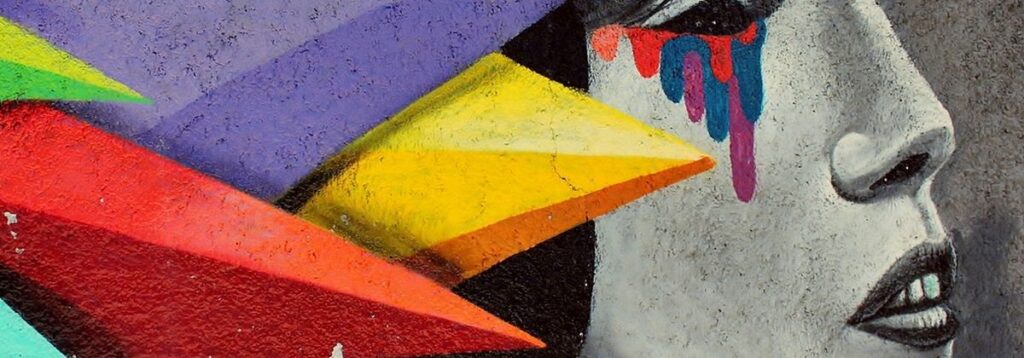 Frauenkopf seiltich als Graffity, am Hinterkopf ein buntes kopfbedeckendes Kostüm.