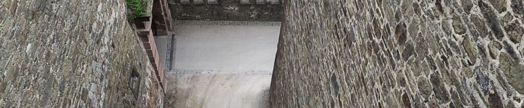 Blick in den Burggraben, an sehr hohen Mauern nach unten blickend.