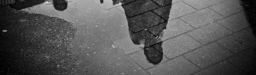 Fußgänger spiegeln sich in Pfützen auf der Straße.