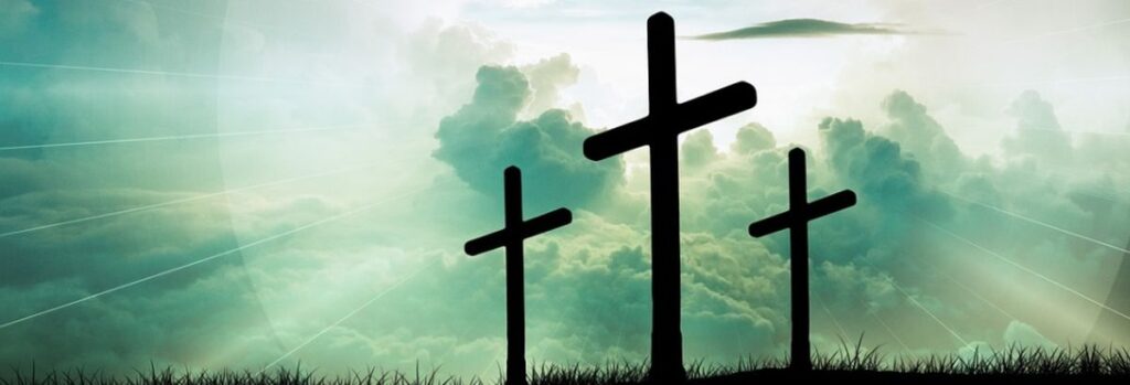 Drei Holzkreuze vor stahlendem Himmel. Die symbolische Bedeutung ist, dass am Kreuz Jesus Christus die Errettung für alle Menschen, die glauben wollen, vollbracht hat.